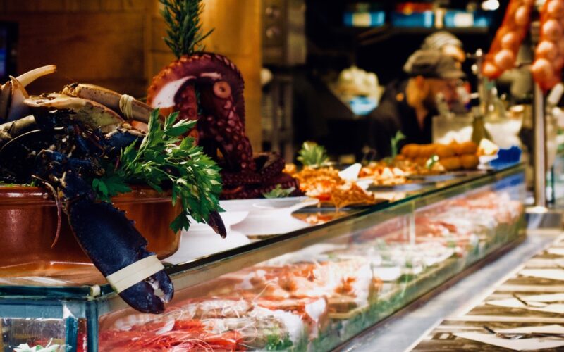 Una vetrina di un mercatino di Natale ricca di cibi freschi da acquistare come salumi, pesci, crostacei