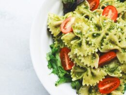 Un piatto di pasta a forma di farfalle condite con pesto verde e pomodorini, serviti su un letto di insalata verde