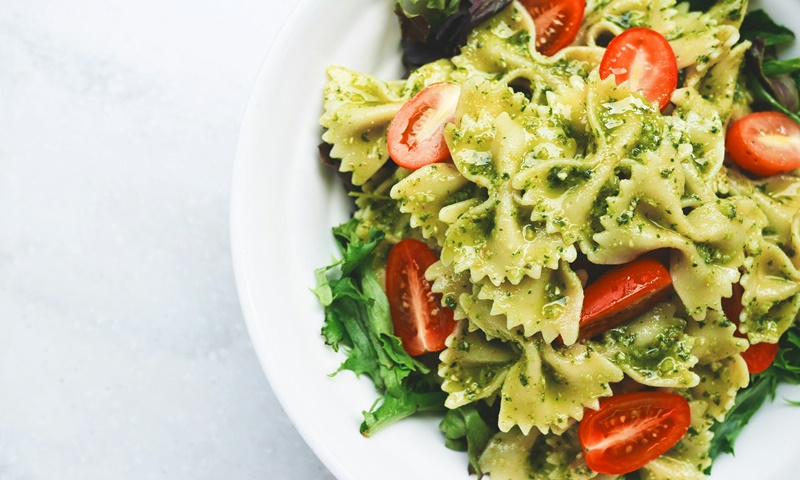 Un piatto di pasta a forma di farfalle condite con pesto verde e pomodorini, serviti su un letto di insalata verde