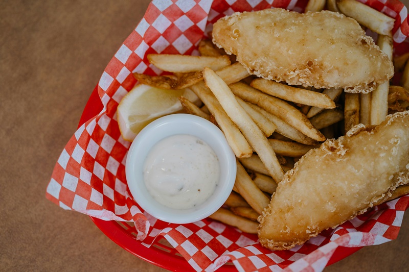 Una porzione di fish & chips, pesce fritto e patatine, servite in un cesto rosso da fast food