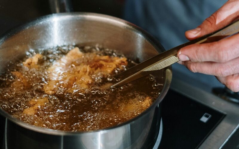 Una pentola piena di olio bollente e del cibo che sta friggendo formando una serie di bollicine in superficie