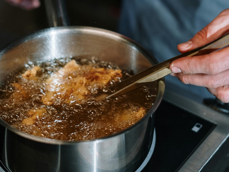 Una pentola piena di olio bollente e del cibo che sta friggendo formando una serie di bollicine in superficie