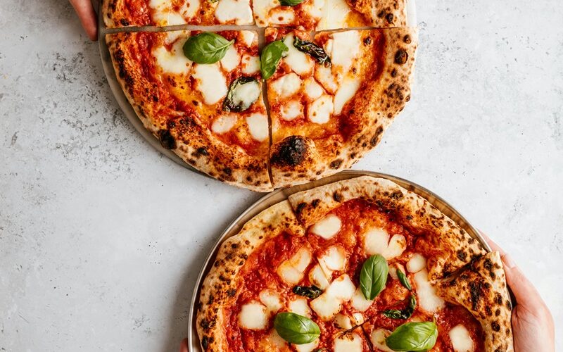 Due pizze napoletane con salsa di pomodoro, mozzarella e basilico su un piano da lavoro in marmo bianco