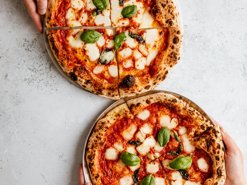 Due pizze napoletane con salsa di pomodoro, mozzarella e basilico su un piano da lavoro in marmo bianco