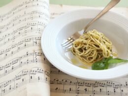 un piatto di spaghetti al pesto è poggiato su un quaderno di musica, in particolare su due pagine che contengono degli spartiti musicali. è una metafora del cibo nella musica