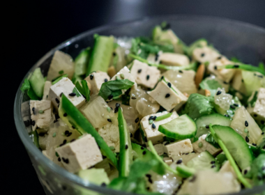 L'immagine mostra una sezione di una bowl di vetro che contiene un'insalata fredda di tofu, semi di sesamo nero, zucchine a julienne e altre verdure