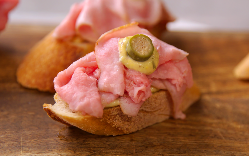 un cicchetto veneziano composto da una fetta di pane, carpaccio di manzo, salsa tonnata e un'oliva come decorazione