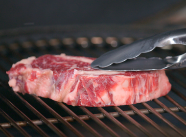 Una fetta di carne poggiata su una griglia accesa