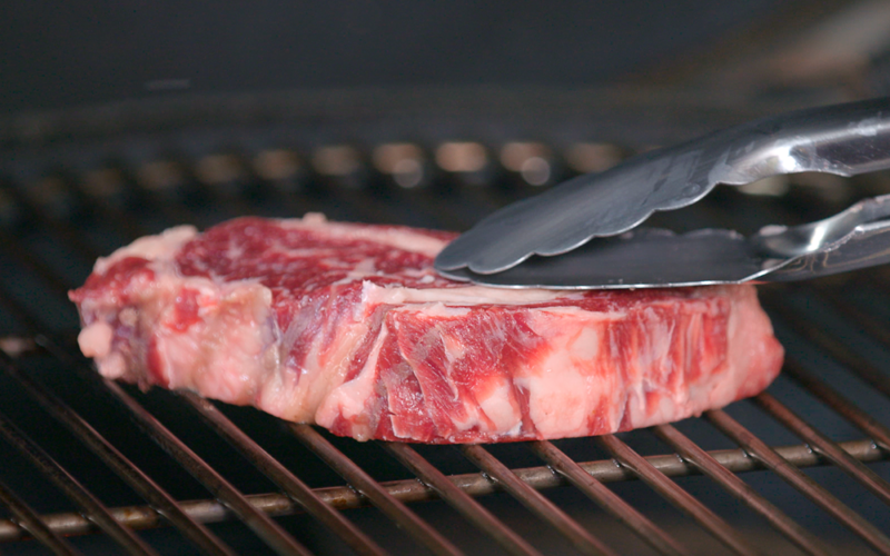Una fetta di carne poggiata su una griglia accesa