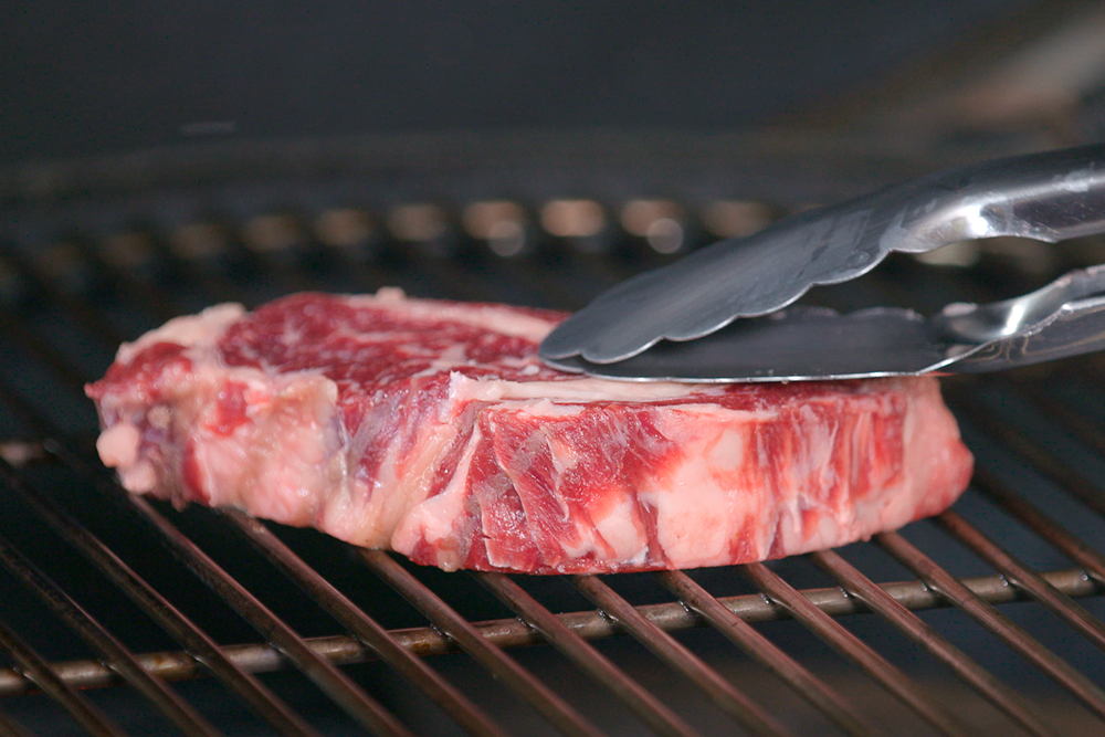 Una fetta di carne poggiata su una griglia accesa
