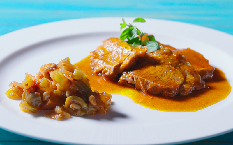 un piatto di caponata siciliana su un tavolo celeste