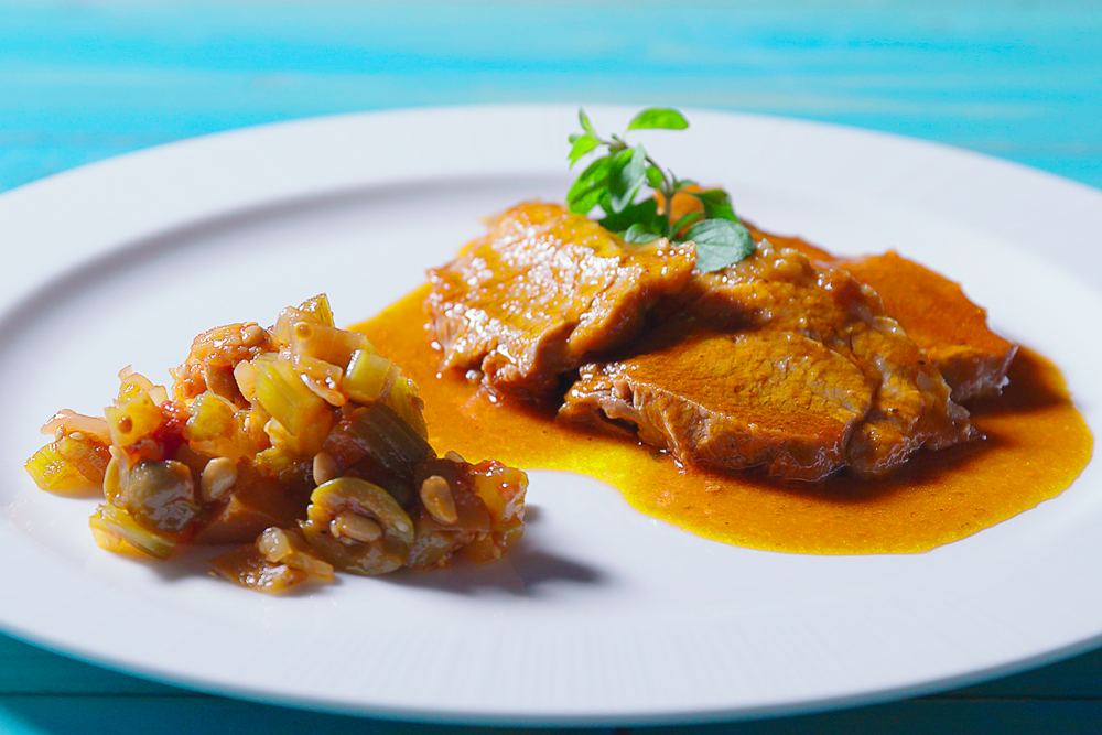un piatto di caponata siciliana su un tavolo celeste