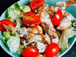 una bowl di caesar salad con pomodori, insalata, pollo e salsa caesar