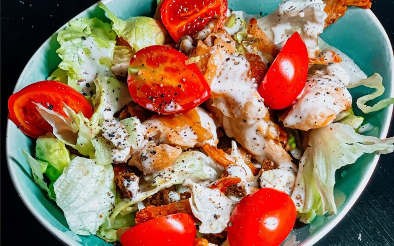 una bowl di caesar salad con pomodori, insalata, pollo e salsa caesar