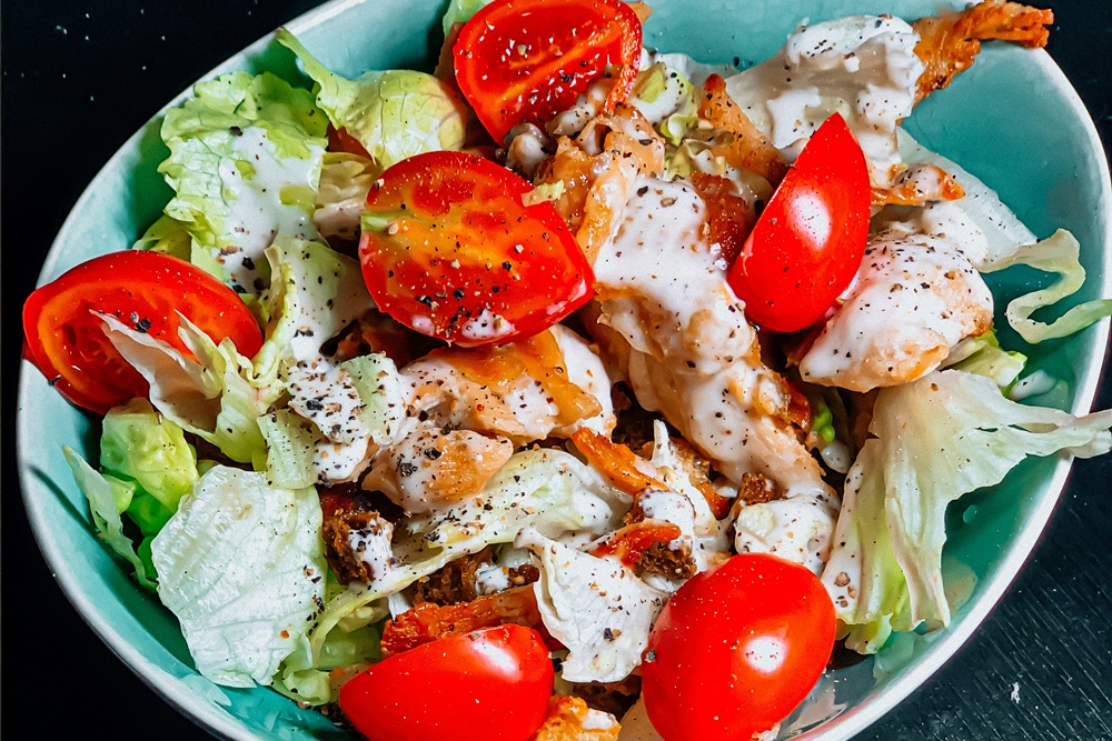 una bowl di caesar salad con pomodori, insalata, pollo e salsa caesar