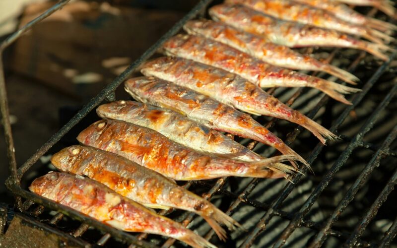 una griglia su cui sta cuocendo del pesce, precisamente delle sardine