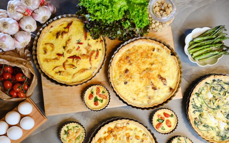 una tavola imbanita con diverse quiche lorraine di diversi gusti e dimensioni