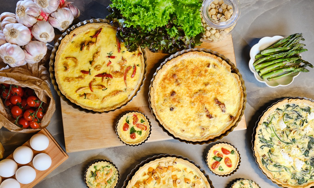 una tavola imbanita con diverse quiche lorraine di diversi gusti e dimensioni