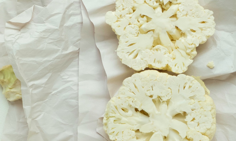 un cavolfiore bianco crudo tagliato a mo di bistecca posato su un panno bianco e pronto da mangiare crudo