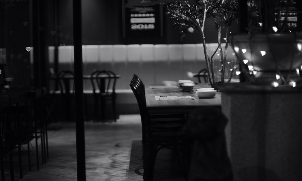 Una foto in bianco e nero in cui si intravede un tavolo di un ristorante per una cena da soli per uno