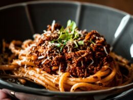 un piatto nero che contiene degli spaghetti conditi con un ragù uno dei primi piatti napoletani