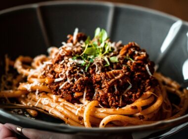un piatto nero che contiene degli spaghetti conditi con un ragù uno dei primi piatti napoletani