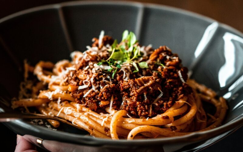 un piatto nero che contiene degli spaghetti conditi con un ragù uno dei primi piatti napoletani