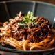 un piatto nero che contiene degli spaghetti conditi con un ragù uno dei primi piatti napoletani