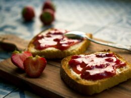 Un tagliere in legno su cui sono poggiate due fette di pane tostato su cui è stata spalmata della marmellata di fragole