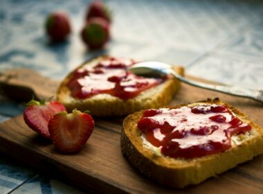 Un tagliere in legno su cui sono poggiate due fette di pane tostato su cui è stata spalmata della marmellata di fragole