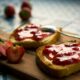 Un tagliere in legno su cui sono poggiate due fette di pane tostato su cui è stata spalmata della marmellata di fragole