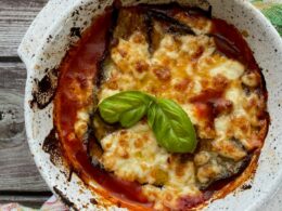 una teglia di parmigiana di melanzane appena sfornata con una foglia di basilico verde
