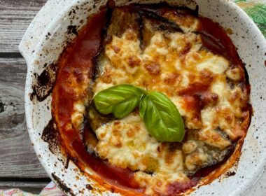 una teglia di parmigiana di melanzane appena sfornata con una foglia di basilico verde