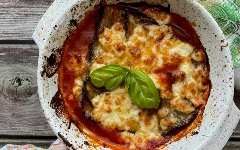 una teglia di parmigiana di melanzane appena sfornata con una foglia di basilico verde