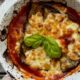 una teglia di parmigiana di melanzane appena sfornata con una foglia di basilico verde