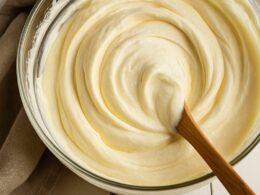 una ciotola che contiene una crema al mascarpone che viene mescolata con un cucchiaio di legno