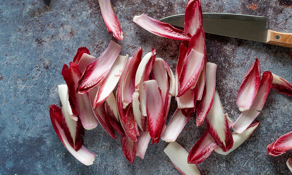 un radicchio spogliato di tutte le sue foglie, poggiato su un tavolo da cucina con accanto un coltello