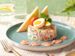 un piatto con una porzione di insalata russa guarnita con una salsa di accompagnamento e delle uova sode sopra