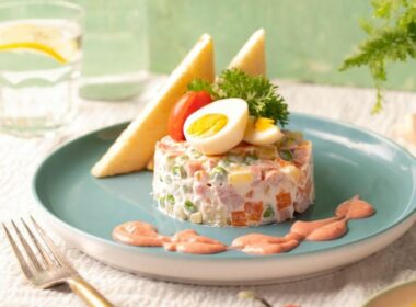 un piatto con una porzione di insalata russa guarnita con una salsa di accompagnamento e delle uova sode sopra