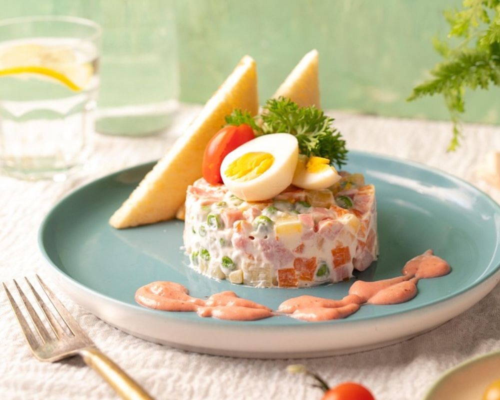 un piatto con una porzione di insalata russa guarnita con una salsa di accompagnamento e delle uova sode sopra