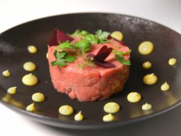 un piatto nero che contiene una tartare condita con delle gocce di maionese sparse sul bordo del piatto