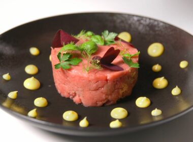 un piatto nero che contiene una tartare condita con delle gocce di maionese sparse sul bordo del piatto