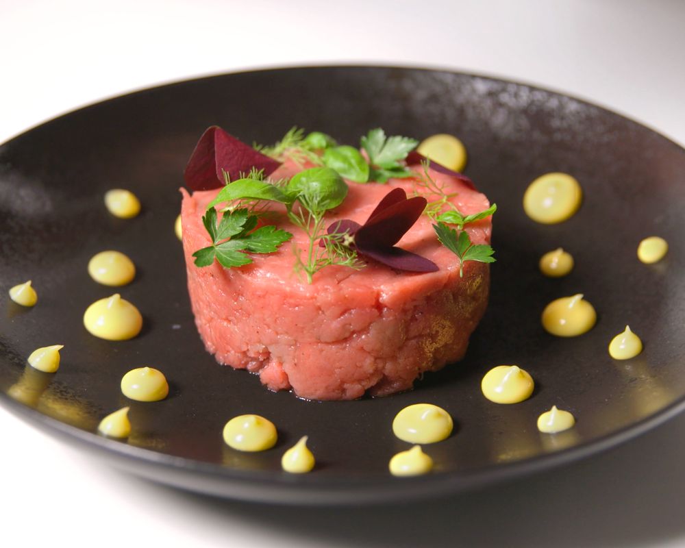 un piatto nero che contiene una tartare condita con delle gocce di maionese sparse sul bordo del piatto