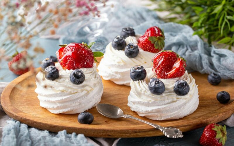 un tagliere in legno su cui sono adagiate tre mini pavlove