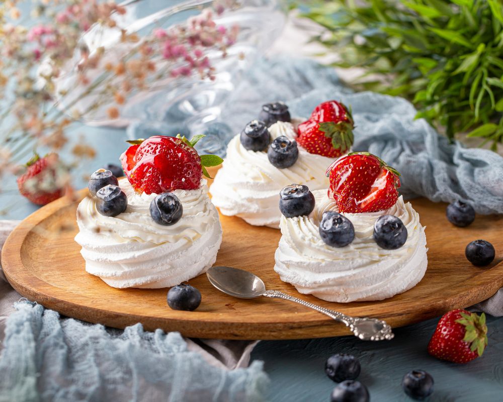 un tagliere in legno su cui sono adagiate tre mini pavlove